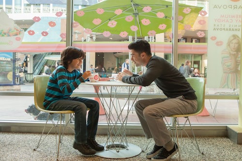 Father and son enjoying two cups of frozen yogurt at a table in front of window