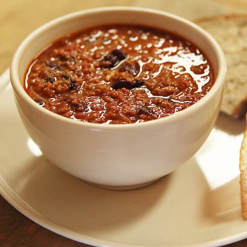 bowl of chili in a white bowl on a white plate with bread slices