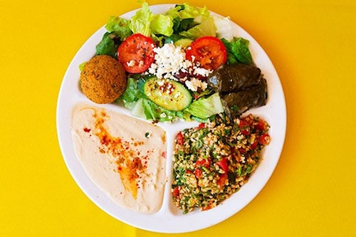 White plate of Mediterranean food with salad and hummus on a yellow table