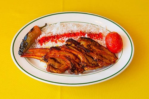 White plate of Mediterranean food with meat and rice on a yellow table