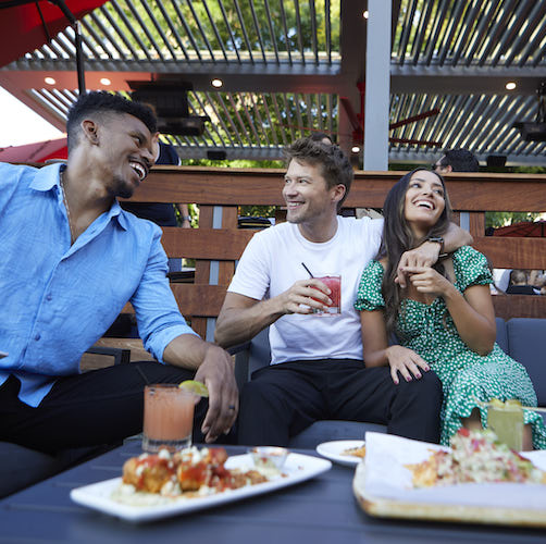 Three people on Finney's Crafthouse patio with appetizers and drinks