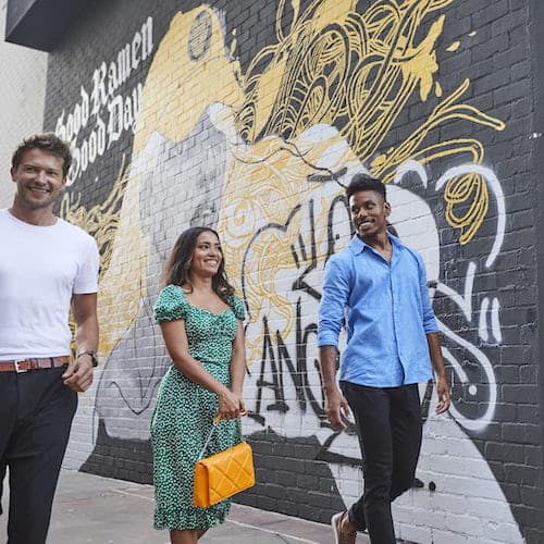 Two men and one women in green dress walking in front of Silverlake Ramen mural