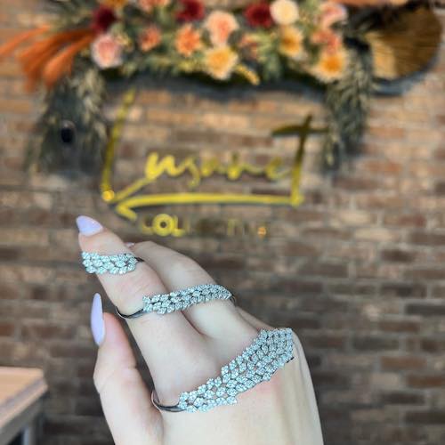 Hand holding rhinestone jewelry in front of brick wall and flowers