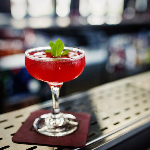 Red cocktail on a brown napkin on top of bar