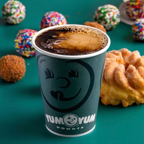 Cup of coffee with Yum Yum Donuts logo and donuts on green table