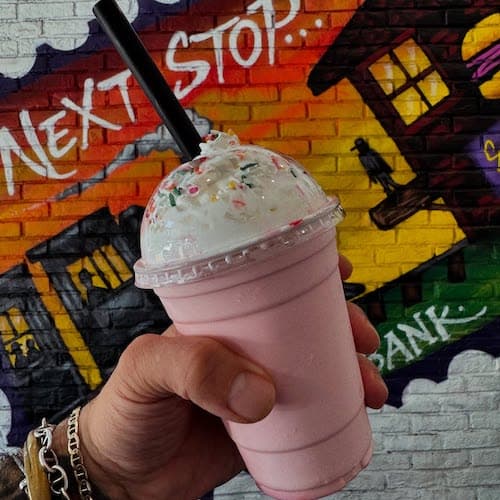 Pink milkshake with whipped cream in front of mural