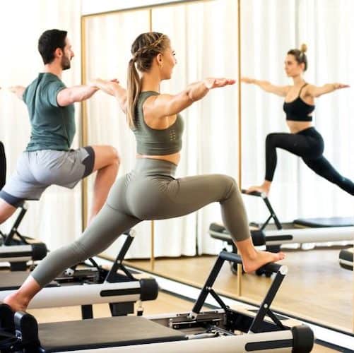 Group of men and women using pilates equipment in front of the mirror