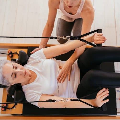 Teacher assisting a woman on a pilates reformer machine