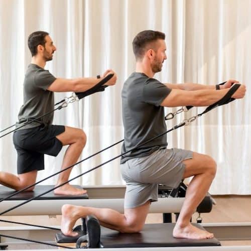 Two men using pilates reformer machines with a white fabrix background