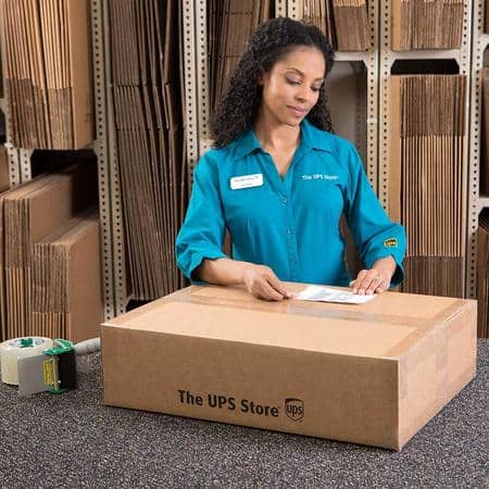 Woman working at UPS Store Burbank in bright blue shirt packing a cardboard box