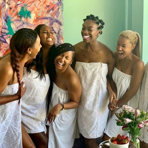 Group of women at a spa wearing white towels with a green wall in the background.