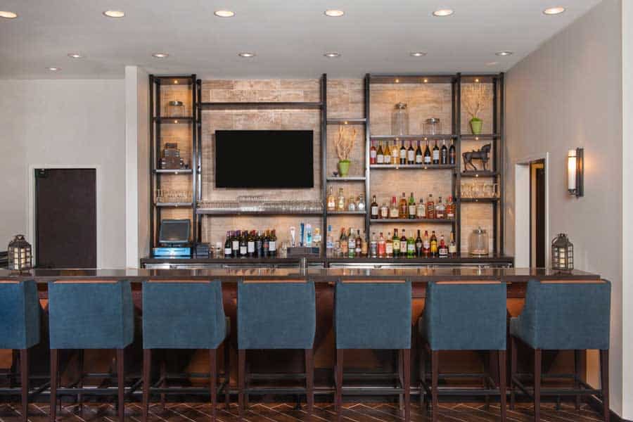 Elegant bar interior with a sleek design, featuring a row of blue barstools, a large TV screen, and shelves stocked with various bottles of liquor and wine. The bar has a modern and inviting atmosphere.