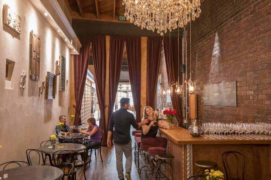 Couple enjoying a drink at an elegant wine bar with chandelier lighting and cozy atmosphere.