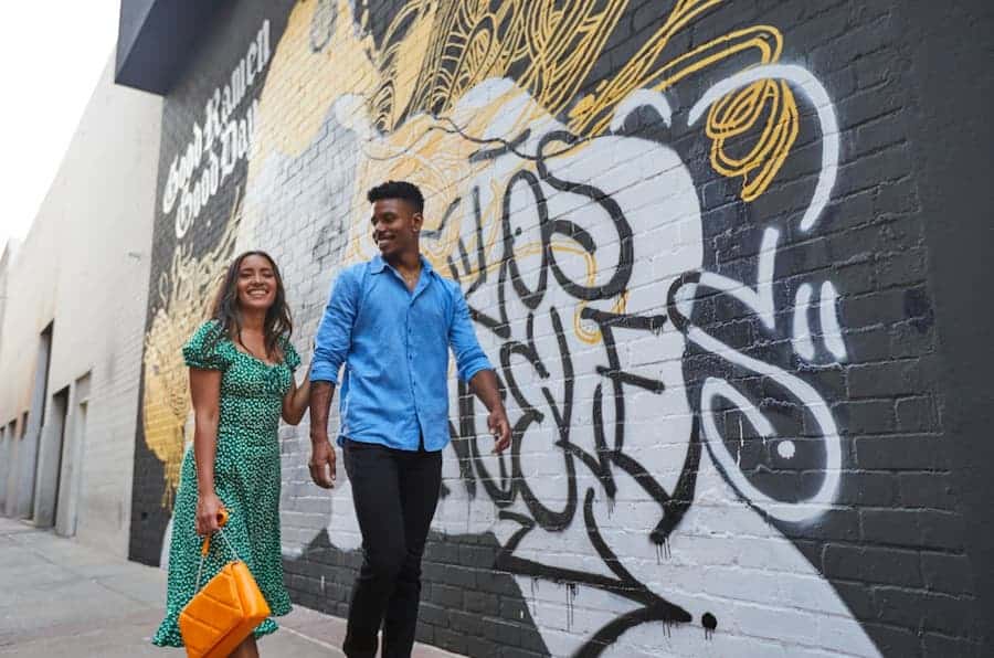 Couple walking in front of colorful street art mural in Downtown Burbank, smiling and holding hands.